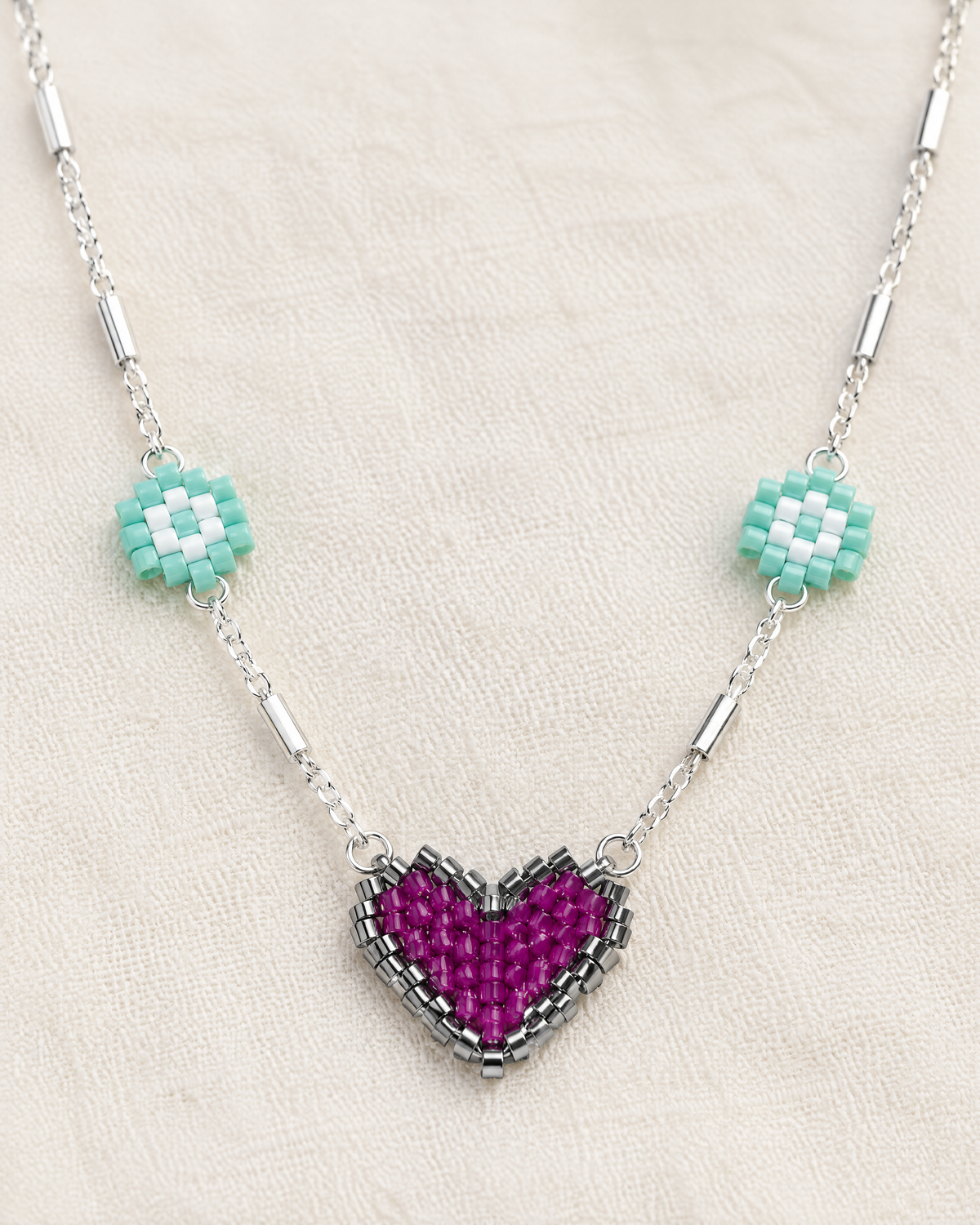 Close-up of the beaded magenta heart pendant and mint daisies on the Daisy Heart Charm Necklace