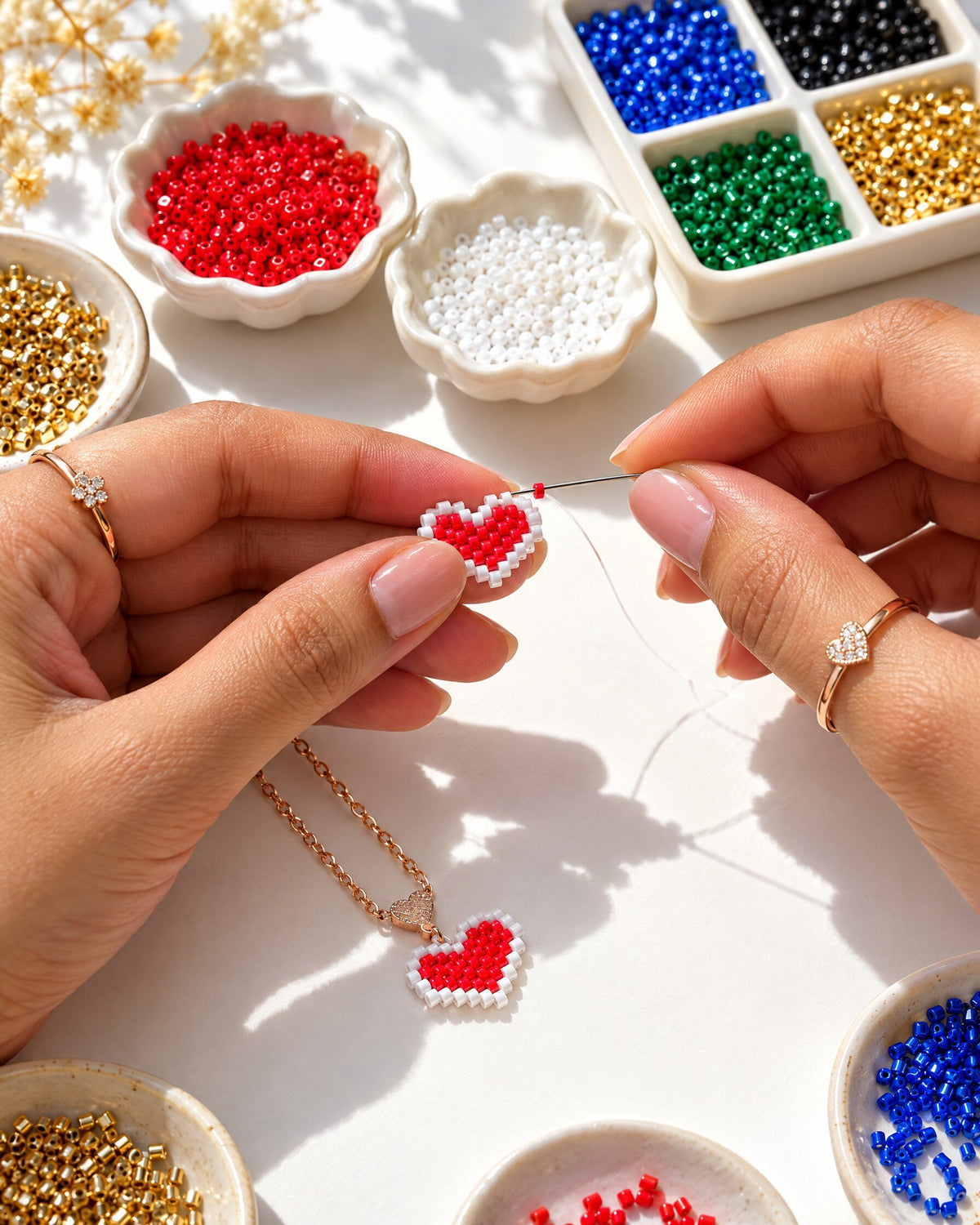 Hands stitching a red beaded heart charm